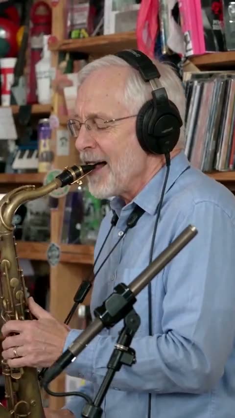 Saxophonist wearing headphones beside office bookshelves in a Tiny Desk AI video reference